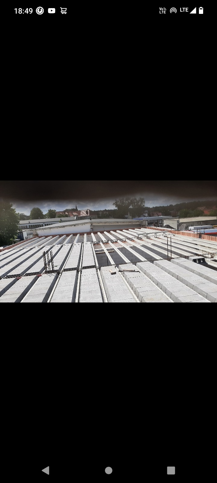 Widok z góry na rozłożone prefabrykowane płyty stropowe z żebrami, przygotowane do zalania betonem na budowie z widokiem na okoliczne budynki.