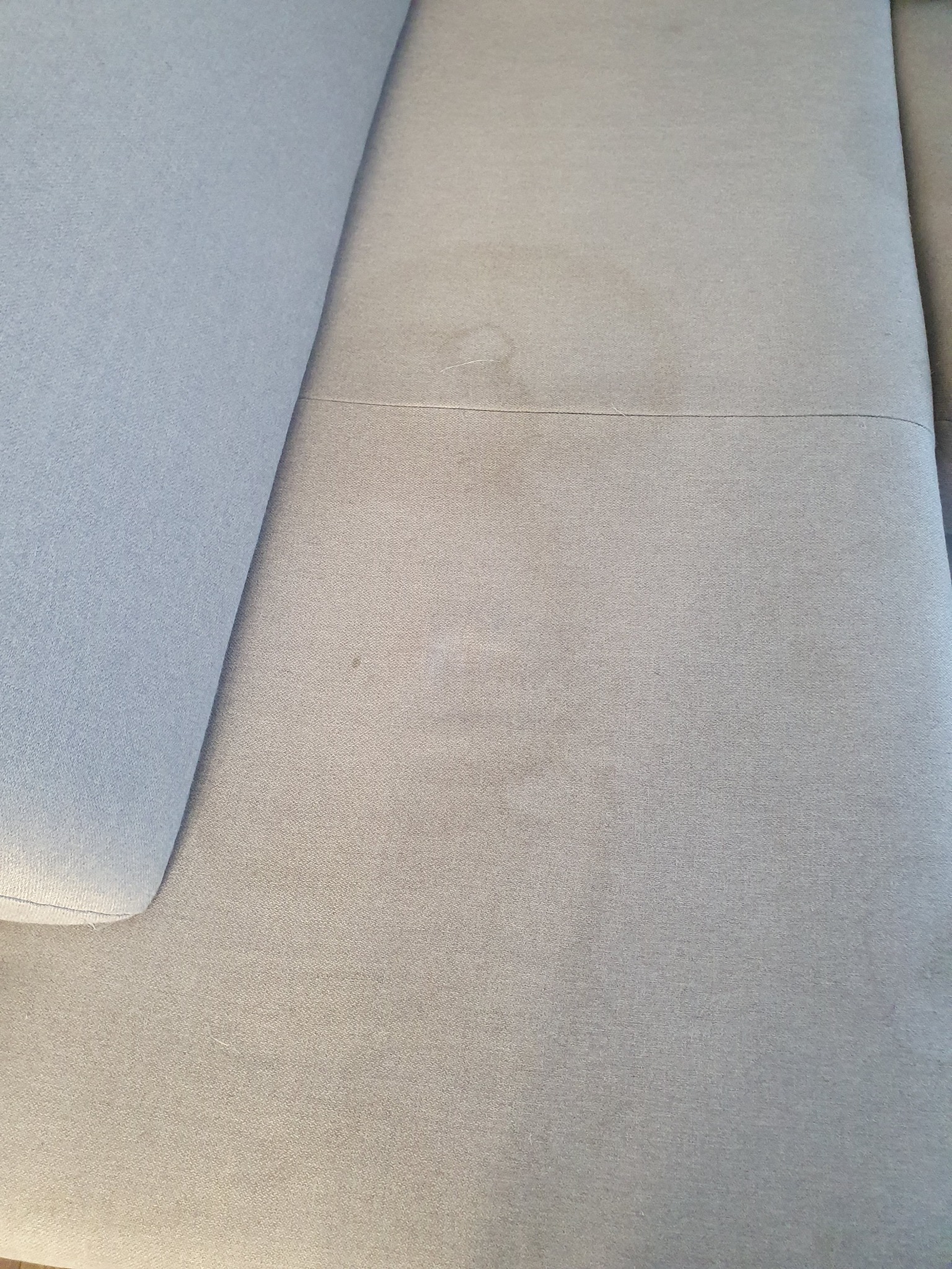 Jasnoszara kanapa z widocznymi plamami na siedzisku, wymagająca czyszczenia.