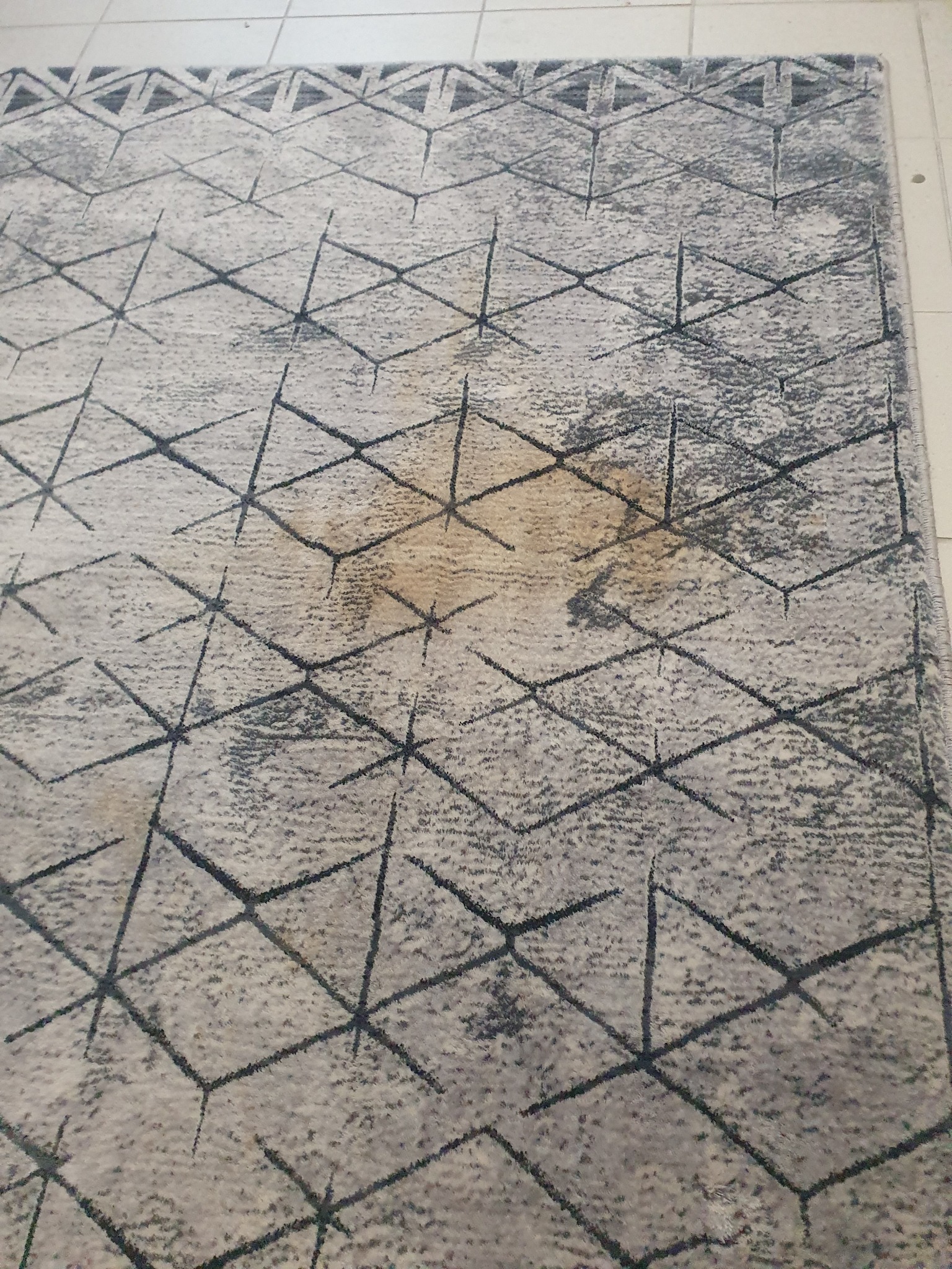 Dywan z geometrycznym wzorem w odcieniach szarości i beżu, widoczna plama na środku.