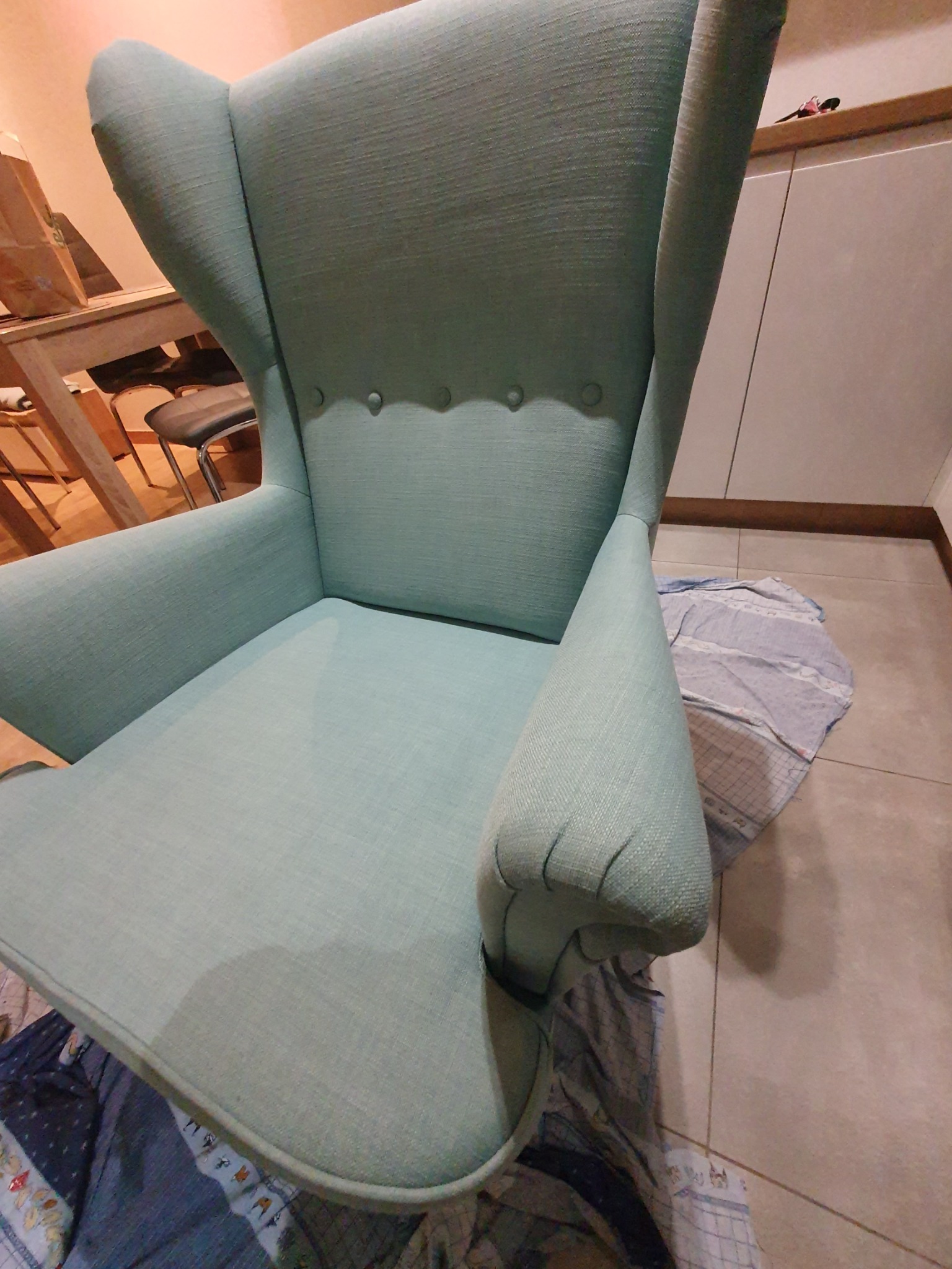 Turkusowy fotel typu uszak na podłodze zabezpieczonej tkaniną, przygotowany do czyszczenia lub po czyszczeniu, widoczne plamy na tkaninie pod fotelem.
