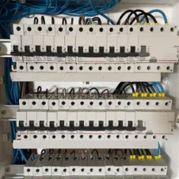 Rozdzielnica elektryczna z zainstalowanymi bezpiecznikami i podłączonymi przewodami o różnych kolorach, z numeracją markerem na obudowach bezpieczników.