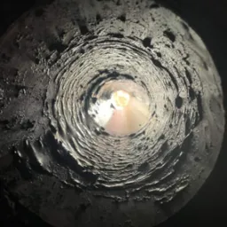 Wnętrze komina w Trzebuchowie, widok od dołu w górę, z widocznymi osadami i światłem na końcu.