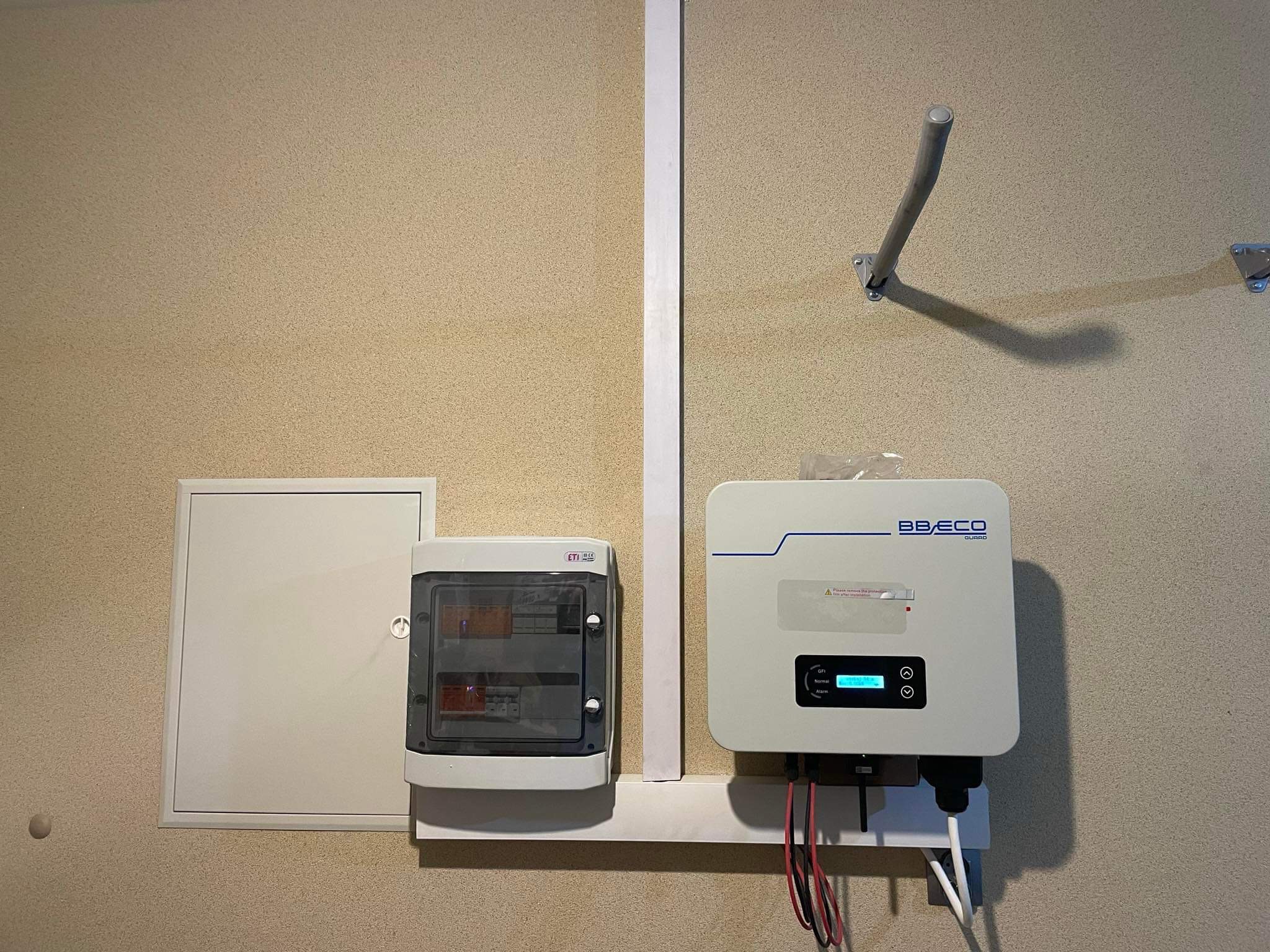 Biały inwerter BB ECO GUARD zamontowany na ścianie obok skrzynki elektrycznej ETI z widocznymi bezpiecznikami, instalacja wewnątrz budynku.