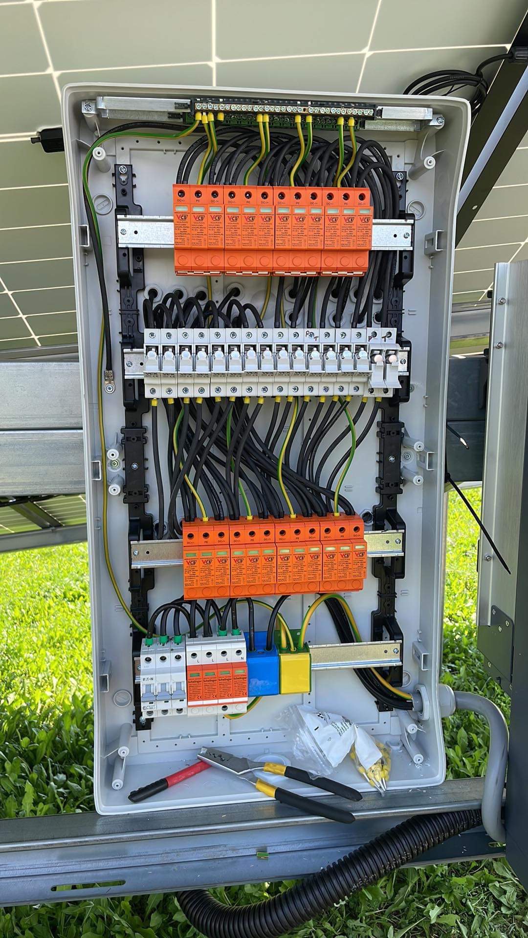 Otwarta skrzynka elektryczna z zabezpieczeniami przepięciowymi w kolorze pomarańczowym, widoczne czarne i żółto-zielone przewody, narzędzia do pracy przy instalacji elektrycznej leżące wewnątrz...