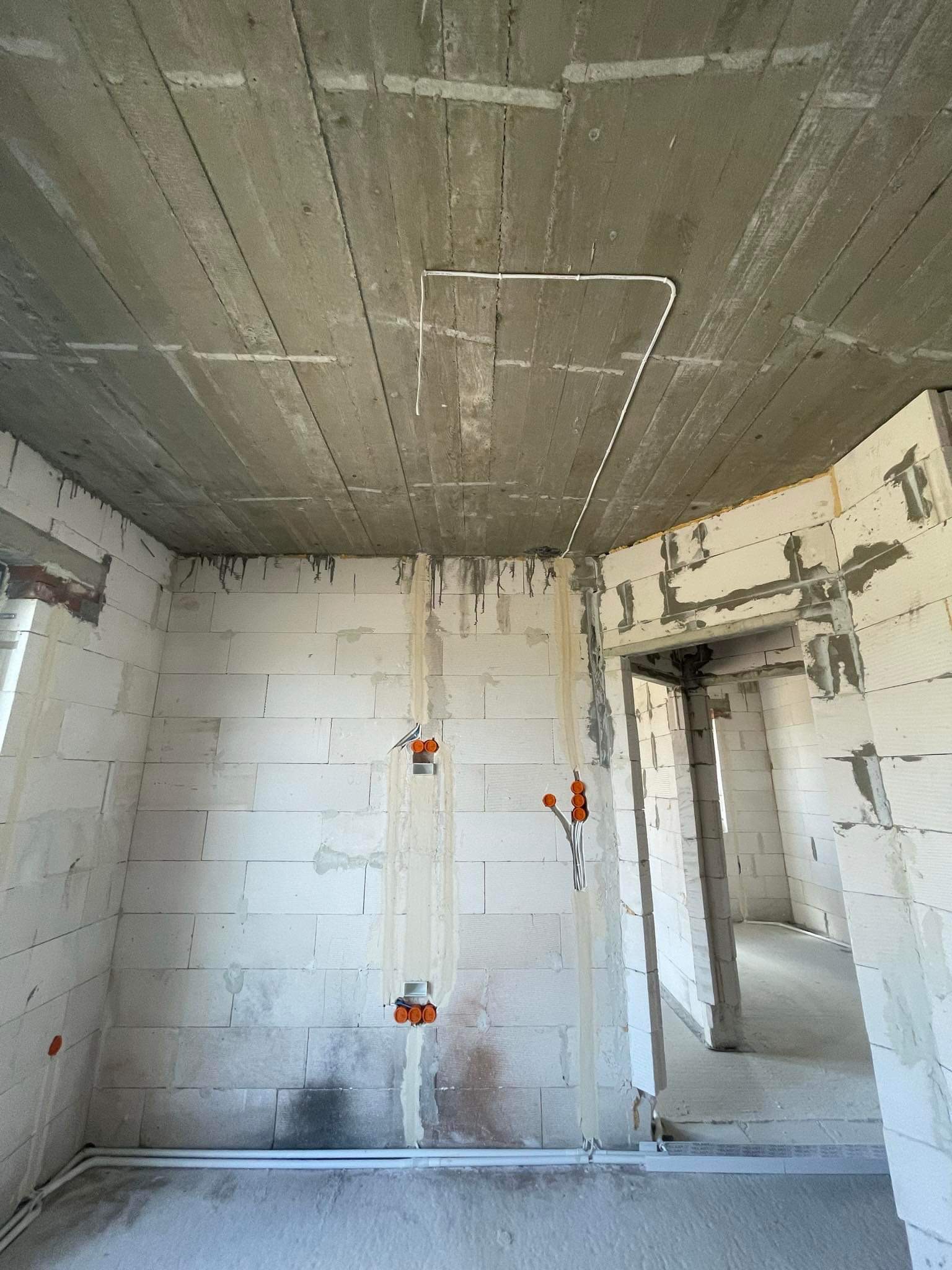 Surowy stan wnętrza budynku w trakcie prac instalacyjnych: widoczne kable elektryczne prowadzone po suficie i w ścianach, puszki instalacyjne wmurowane w białe ściany z betonu komórkowego, betonowy...