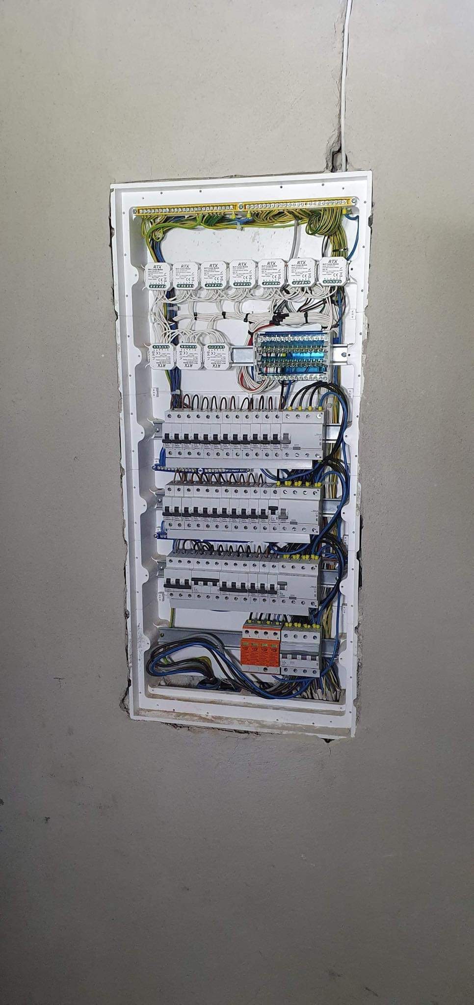 Rozdzielnica elektryczna wnękowa, z widocznymi bezpiecznikami, przewodami i elementami sterującymi, zamontowana w surowej ścianie.