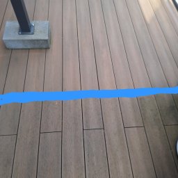 LAVENDA Ewa Samul - Częściowy widok drewnianego tarasu z widocznym słupkiem balustrady i zaznaczoną linią, być może wskazującą obszar do czyszczenia lub renowacji.