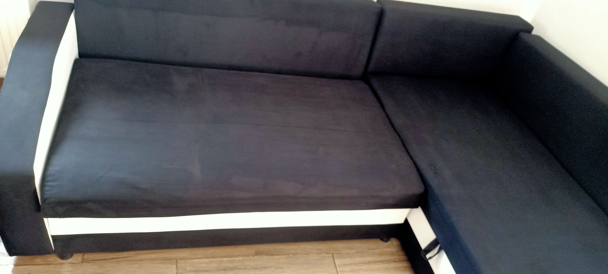 Ciemnogranatowa kanapa narożna z białymi elementami, widok z góry pod kątem, na podłodze panele.