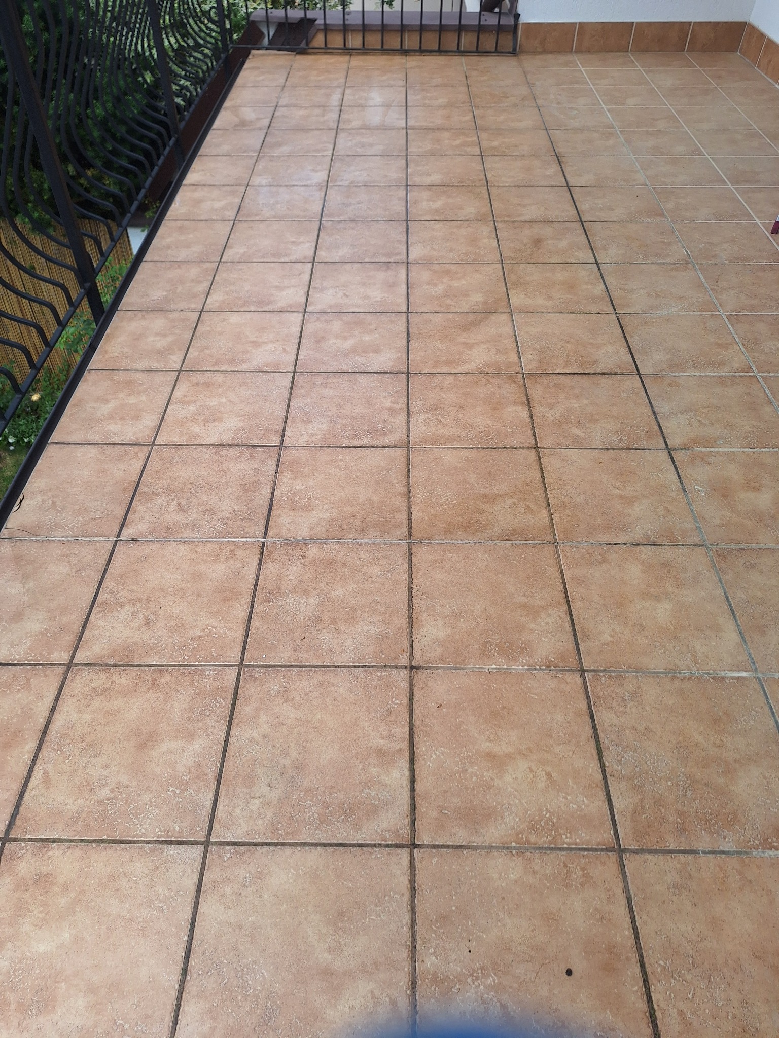 Kafelki podłogowe na balkonie z czarną, ozdobną balustradą, widok z góry, z lekkim zabrudzeniem w fugach.