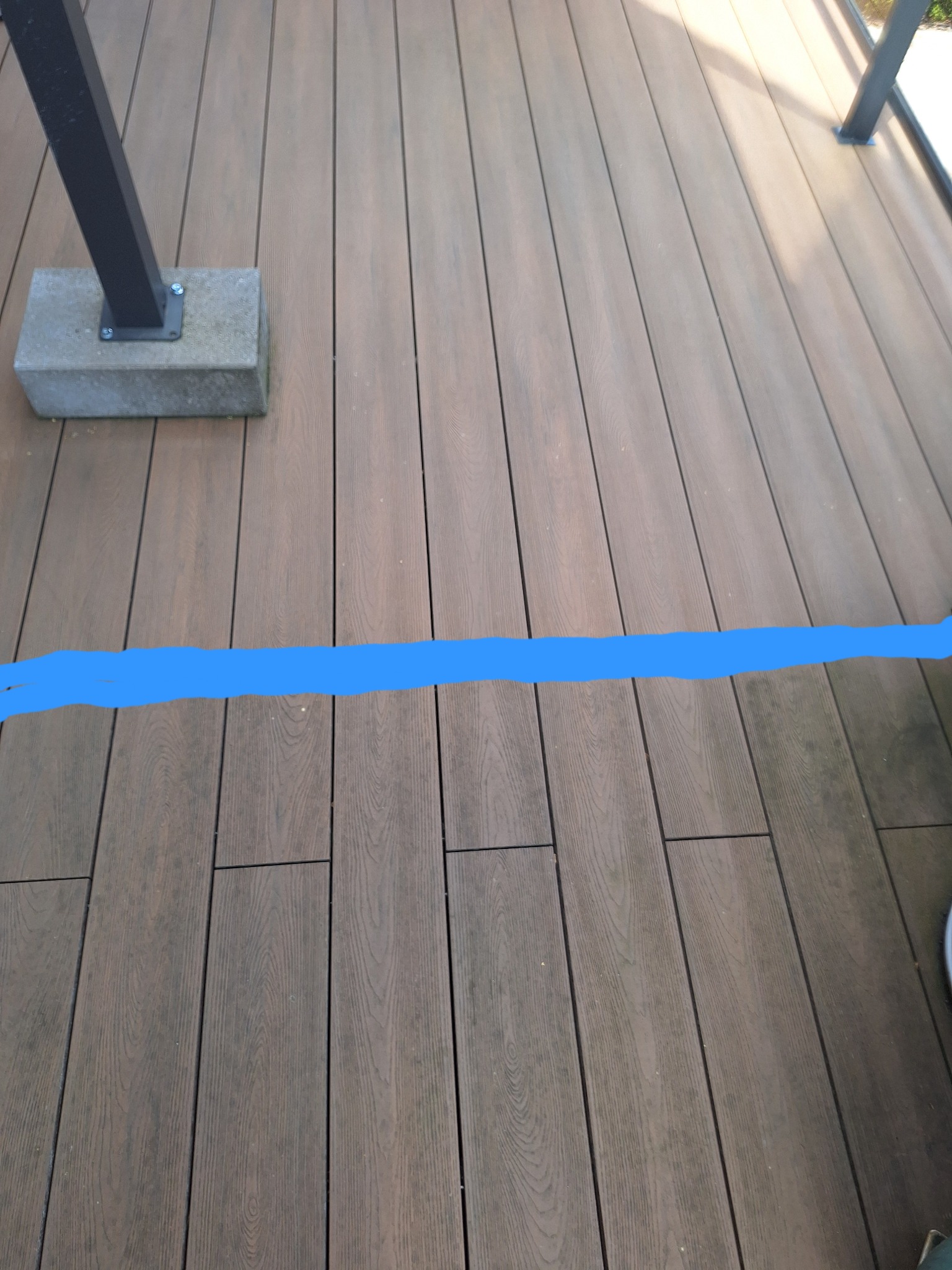 Częściowy widok drewnianego tarasu z widocznym słupkiem balustrady i zaznaczoną linią, być może wskazującą obszar do czyszczenia lub renowacji.