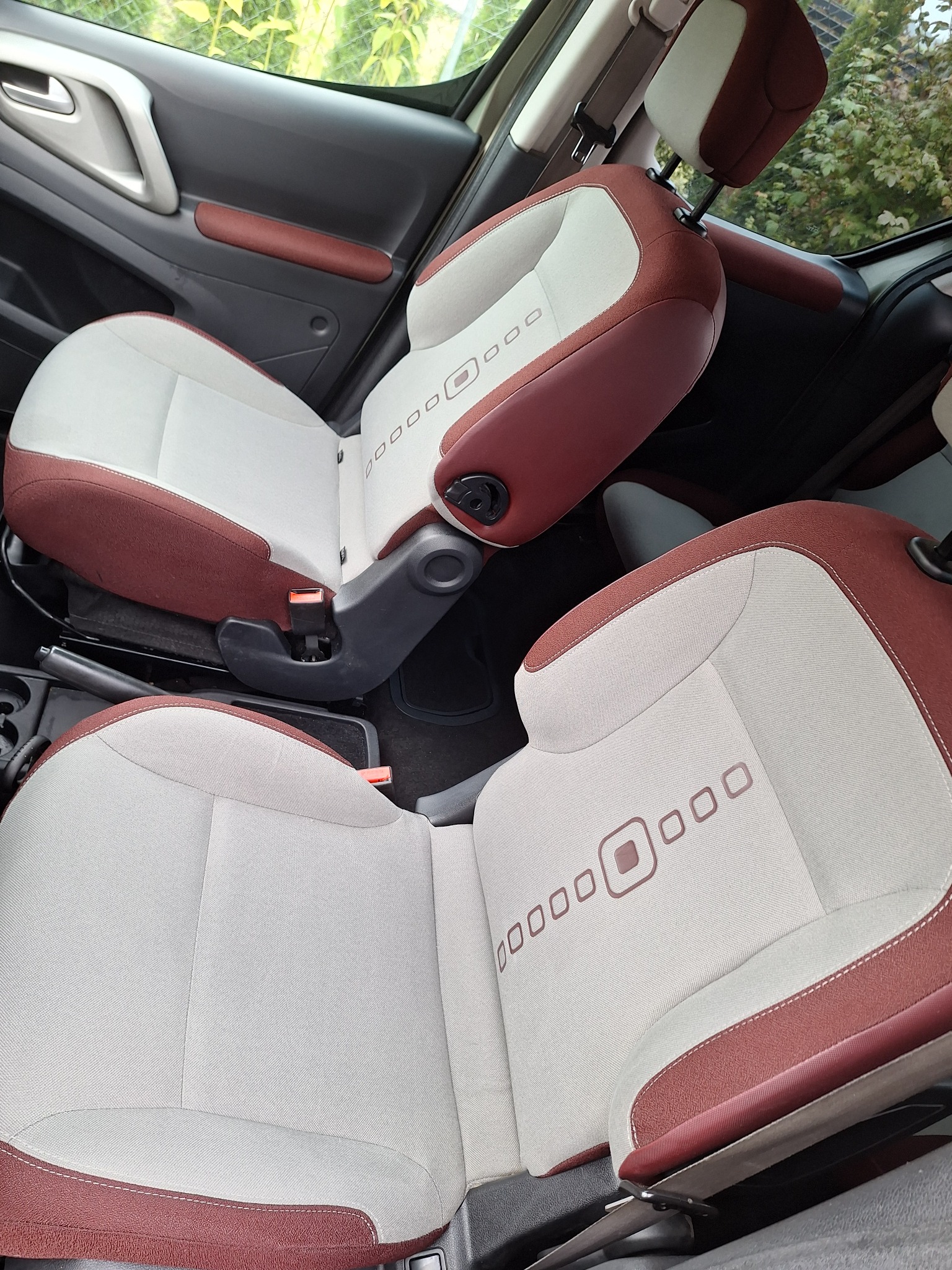 Jasne, dwukolorowe fotele samochodowe z bordowymi akcentami i geometrycznym wzorem. Widok z góry na czyste, zadbane wnętrze pojazdu.