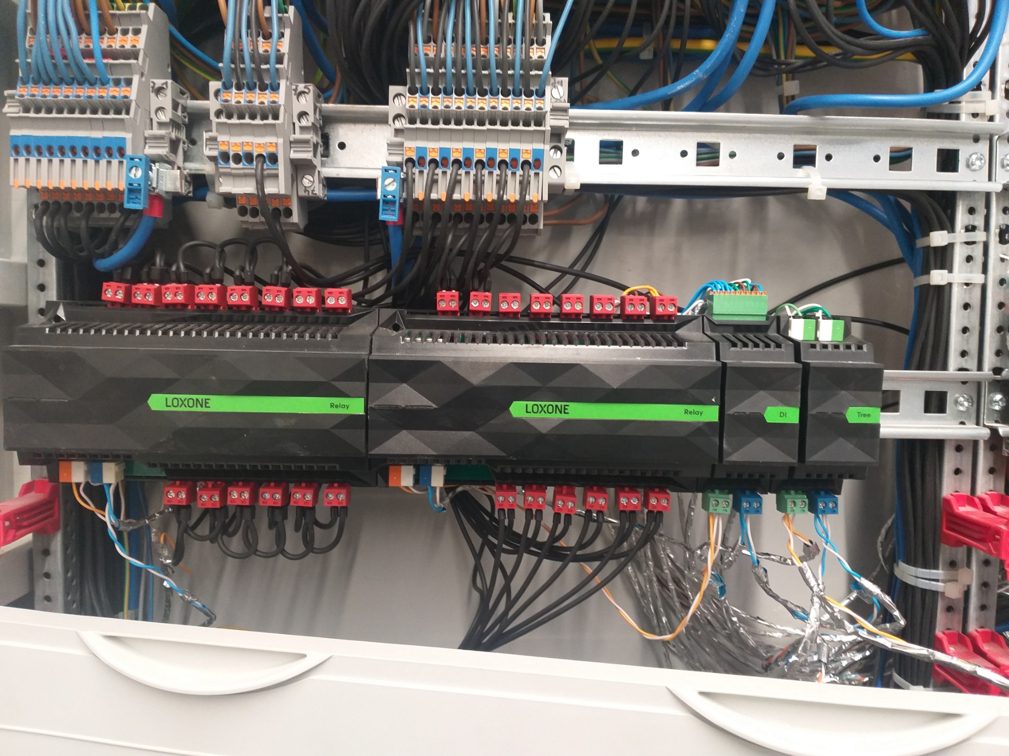 Rozdzielnica elektryczna z modułami Loxone Relay i DI Tree, liczne przewody podłączone do listew zaciskowych, widoczne elementy montażowe na szynie DIN.