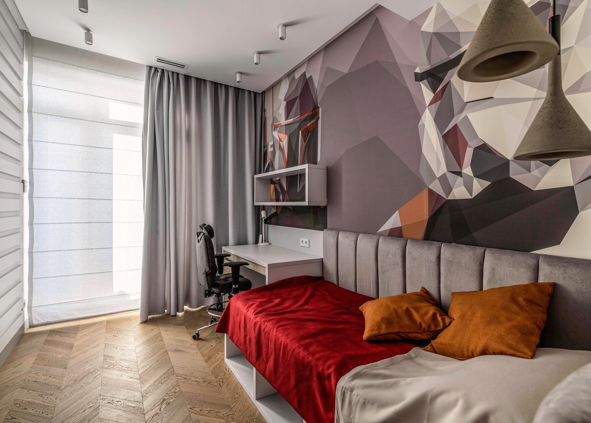 Pokój młodzieżowy z zasłonami rzymskimi i dekoracyjną, szarą zasłoną, biurkiem i łóżkiem z geometrycznym wzorem na ścianie.
