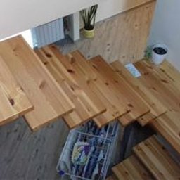 Krzysztof Rożek - Drewniane schody z widoczną konstrukcją wsporczą stopni, prowadzące na poddasze, z koszem na drobiazgi umieszczonym pod biegiem schodów.