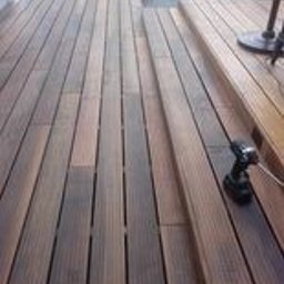 Krzysztof Rożek - Deski tarasowe z drewna egzotycznego ułożone na zewnątrz, widoczna wkrętarka akumulatorowa na tarasie w trakcie montażu, jasne fugi między deskami.