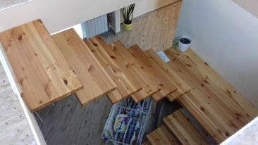 Drewniane schody z widoczną konstrukcją wsporczą stopni, prowadzące na poddasze, z koszem na drobiazgi umieszczonym pod biegiem schodów.