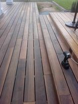 Deski tarasowe z drewna egzotycznego ułożone na zewnątrz, widoczna wkrętarka akumulatorowa na tarasie w trakcie montażu, jasne fugi między deskami.