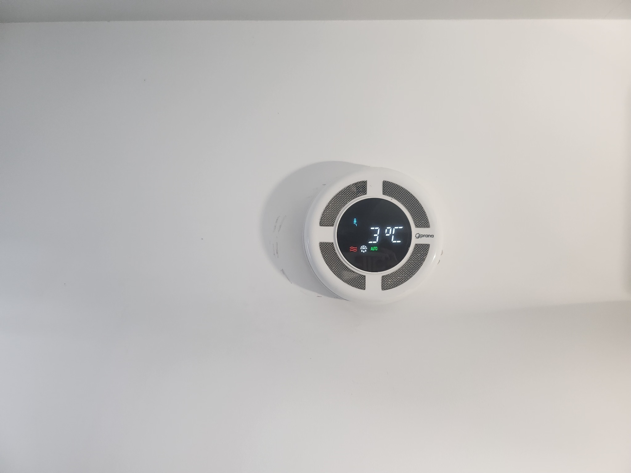 Biały rekuperator Prana zamontowany na białym suficie, wyświetlający temperaturę 3 stopnie Celsjusza w trybie automatycznym.