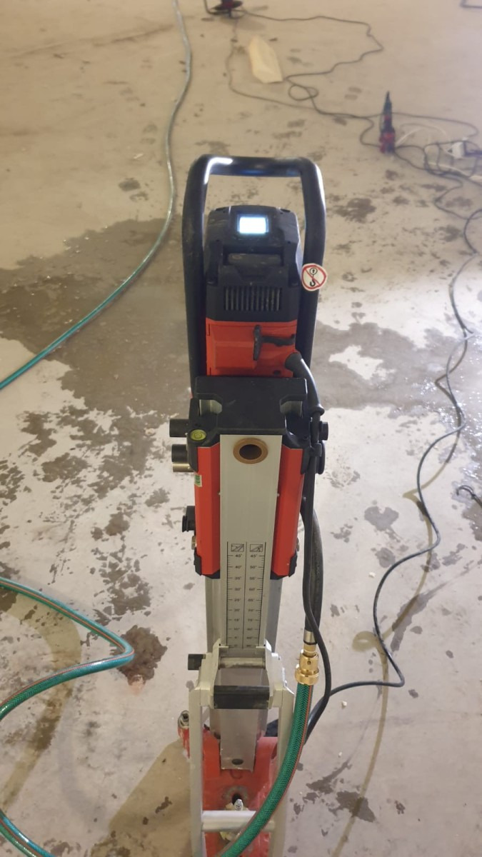 Wiertnica rdzeniowa Hilti DD 150-U na mokro, z widocznym poziomem i wężem doprowadzającym wodę, stojąca na betonowej posadzce z plamami wody.