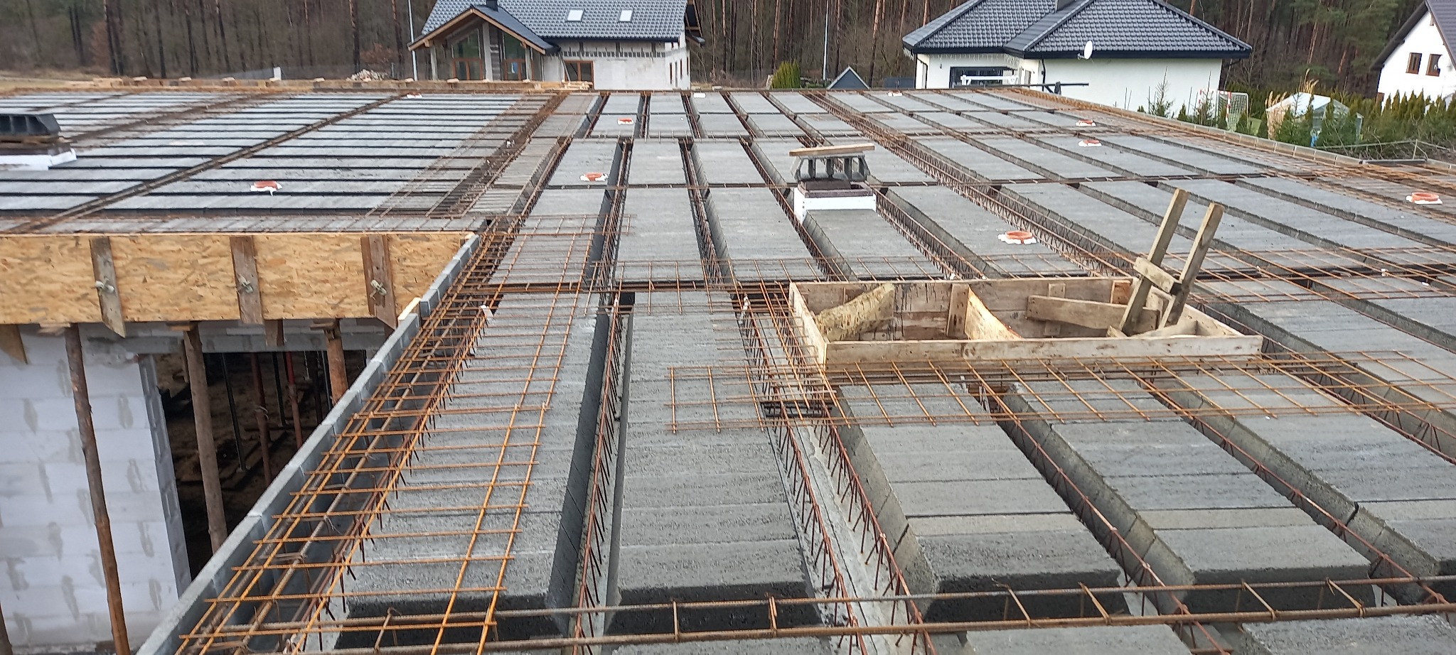 Wiązanie zbrojenia na stropie Teriva z betonowych belek i pustaków szalunkowych podczas budowy domu jednorodzinnego z widocznymi elementami deskowania i zbrojenia wieńca.