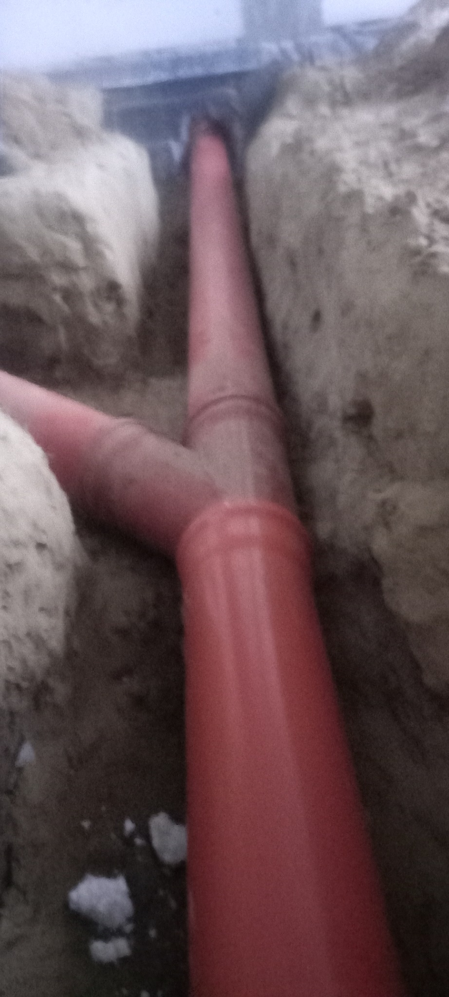 Instalacja czerwonej rury kanalizacyjnej w wykopie fundamentowym, widok z góry na złącze trójnikowe.