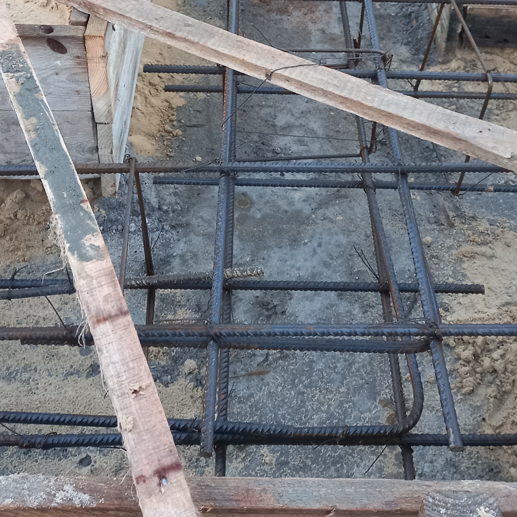 Zbrojenie fundamentu domu z widocznymi prętami stalowymi połączonymi drutem i drewnianym szalunkiem.