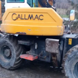 Żółta maszyna budowlana Callmac z dużymi oponami w błotnistym terenie, widoczne schodki i elementy hydrauliczne.