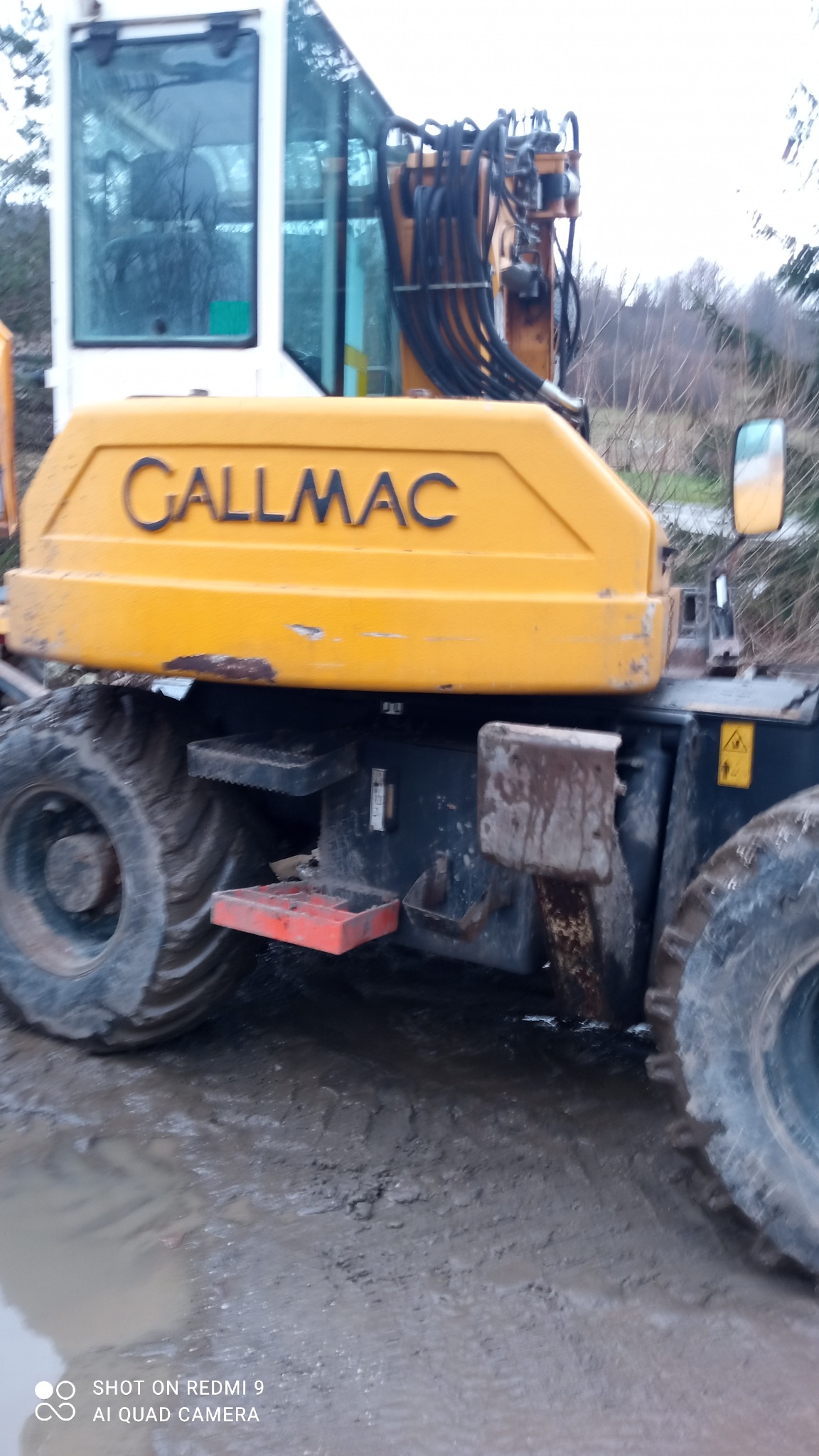 Żółta maszyna budowlana Callmac z dużymi oponami w błotnistym terenie, widoczne schodki i elementy hydrauliczne.