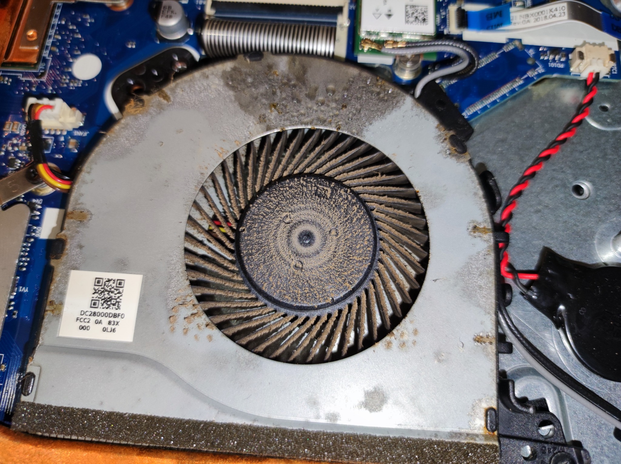 Zabrudzony kurzem wentylator chłodzący wewnątrz laptopa, widoczne elementy płyty głównej i kable