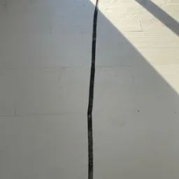 Białe płyty izolacyjne pod wylewkę podłogową z czarnym przewodem w peszlu ułożonym w szczelinie, widoczne ślady butów i cień.