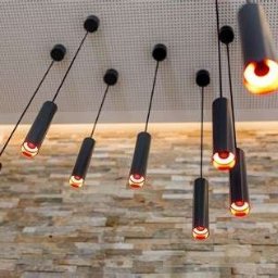 I4Home automatyka domowa Grzegorz Wasil - Nowoczesne oświetlenie sufitowe z cylindrycznymi lampami wiszącymi na cienkich przewodach, emitujące ciepłe światło, na tle ściany z kamienną okładziną.