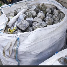 K&K KRZYSZTOF KAZIÓW - Worek z szarą kostką granitową w Cesarzowicach, widoczne nierównomierne bryły i zwinięty arkusz papieru na wierzchu.