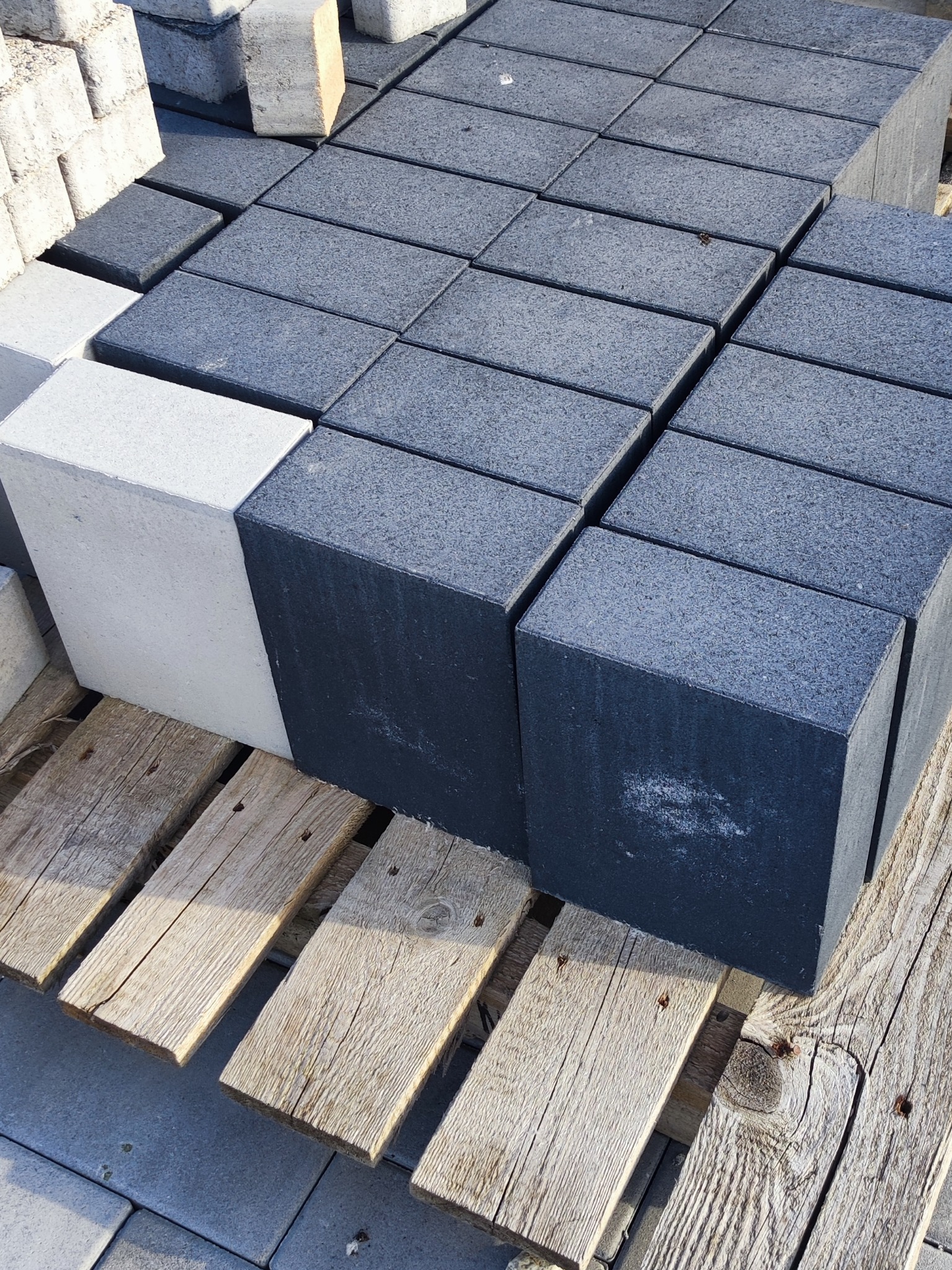 Szare i białe bloczki ułożone na drewnianej palecie, widoczne ślady użytkowania palety.