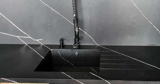 Czarny blat kuchenny z białymi żyłkami, zintegrowany z czarnym zlewem i ociekaczem, bateria w kolorze czarnym z elastyczną wylewką.