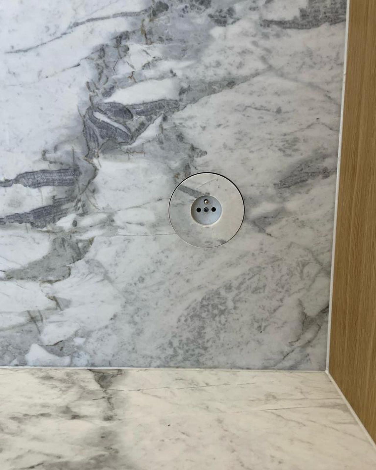 Fragment blatu i ściany z jasnego marmuru z wmontowanym gniazdkiem elektrycznym w Bąkowie.