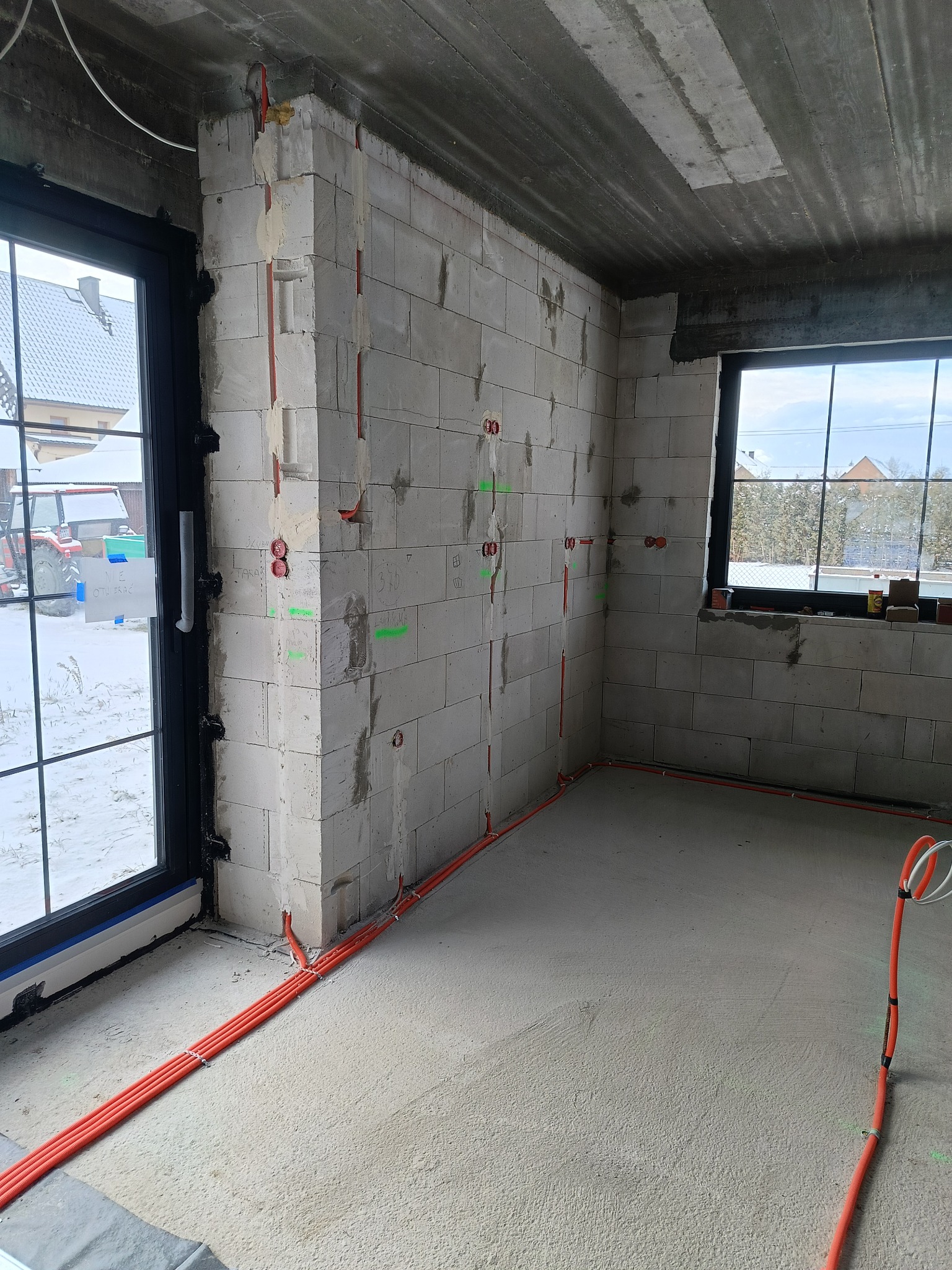 Wnętrze w stanie surowym z widoczną instalacją elektryczną w peszlach, poprowadzoną po ścianach z betonu komórkowego i podłodze. Widoczne puszki elektryczne.