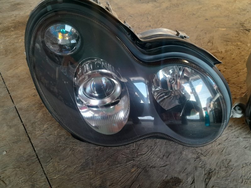 Czarny reflektor samochodowy, prawdopodobnie po tuningu, widoczny w warsztacie we Wrocławiu. Zauważalne rysy na powierzchni klosza.