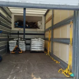 Wnętrze paki transportowej z zabezpieczonym ładunkiem palet z kostką brukową i narzędziem do transportu palet.