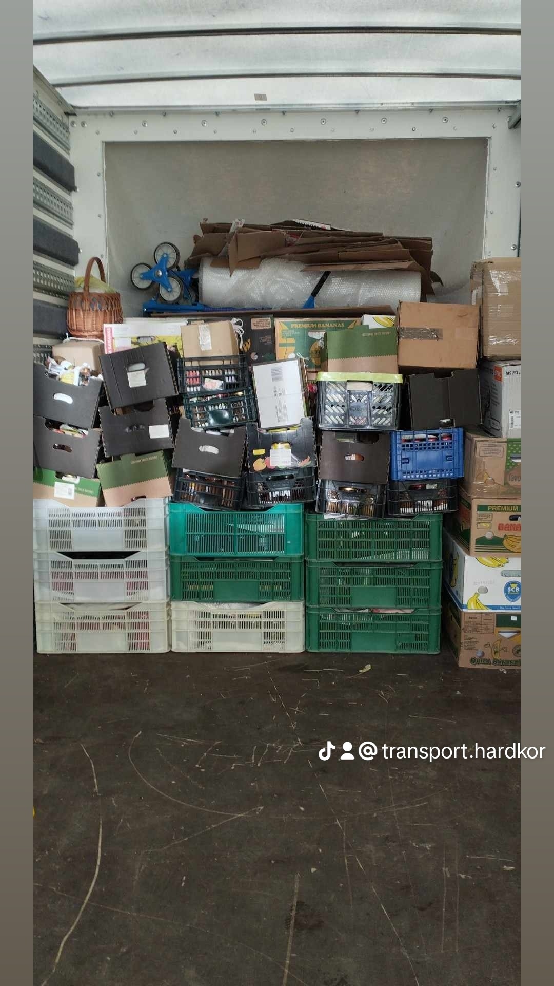Wnętrze furgonetki wypełnione kartonami, skrzynkami z bananami i plastikowymi pojemnikami, przygotowane do transportu. Widoczny wózek do transportu mebli i folia stretch.