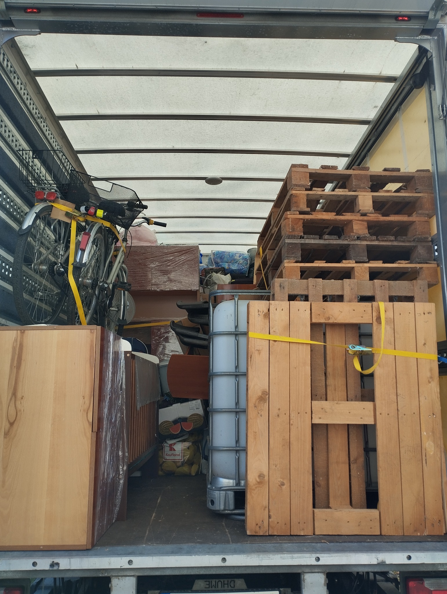 Wnętrze ciężarówki wypełnione meblami, rowerem zabezpieczonym żółtymi pasami, paletami i zbiornikiem na wodę, gotowymi do transportu.