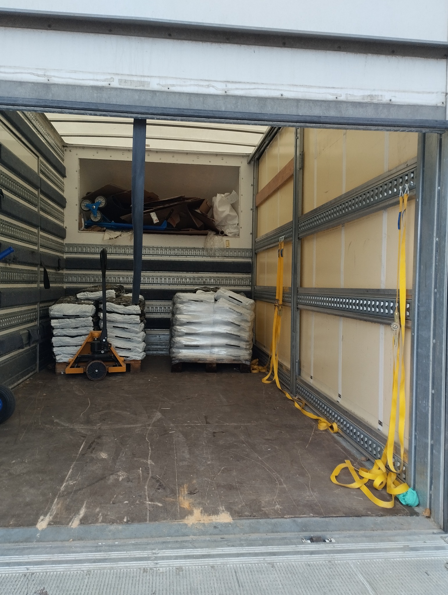 Wnętrze paki transportowej z zabezpieczonym ładunkiem palet z kostką brukową i narzędziem do transportu palet.