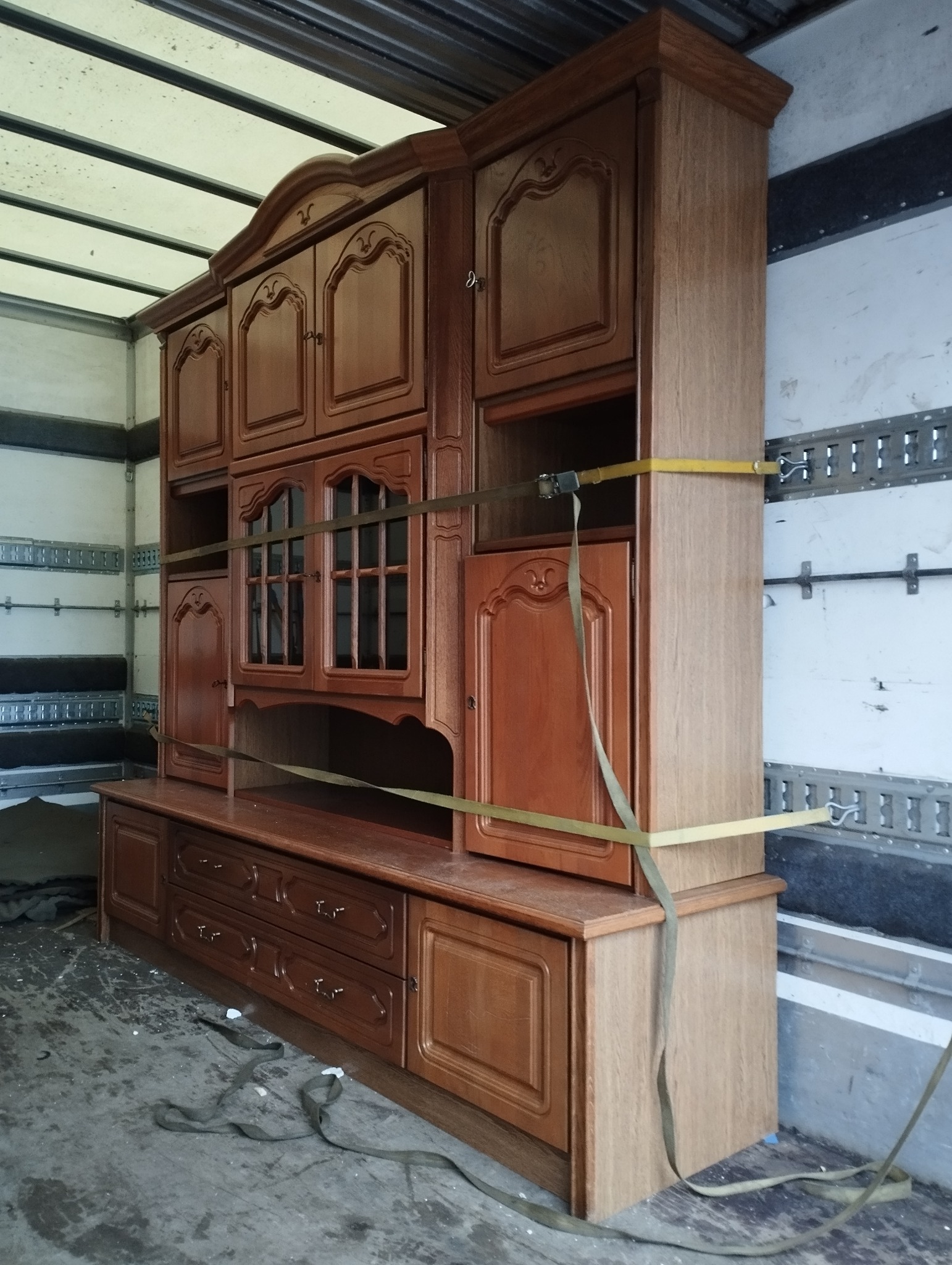 Masywna, drewniana meblościanka zabezpieczona pasami transportowymi wewnątrz przestrzeni ładunkowej pojazdu.