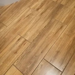 Ułożone pod kątem brązowe płytki podłogowe imitujące drewno, widoczny fragment białej wanny.