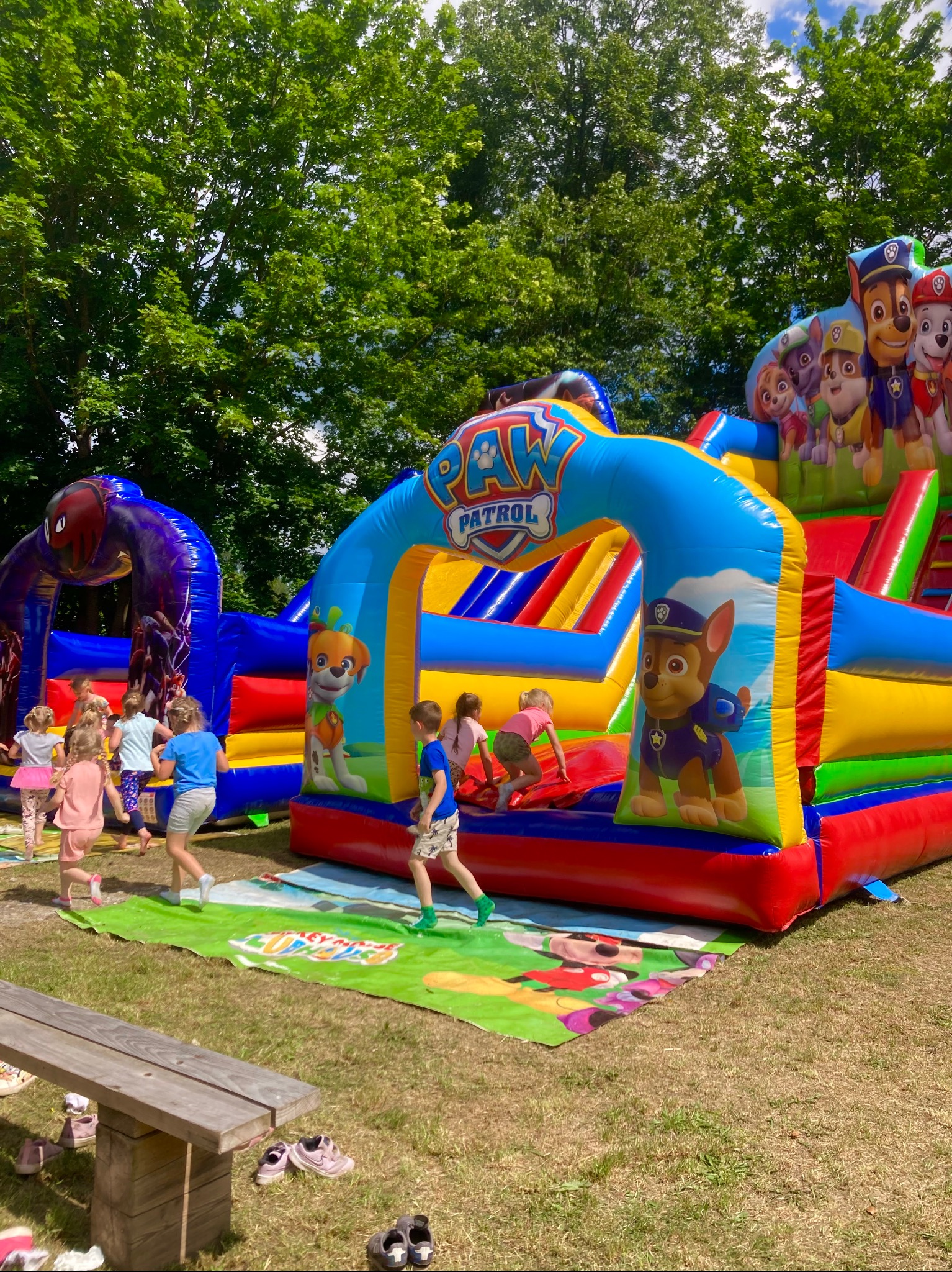 Dzieci bawią się na kolorowym, dmuchanym placu zabaw z motywem bajki Psi Patrol, ustawionym na trawie w plenerze.