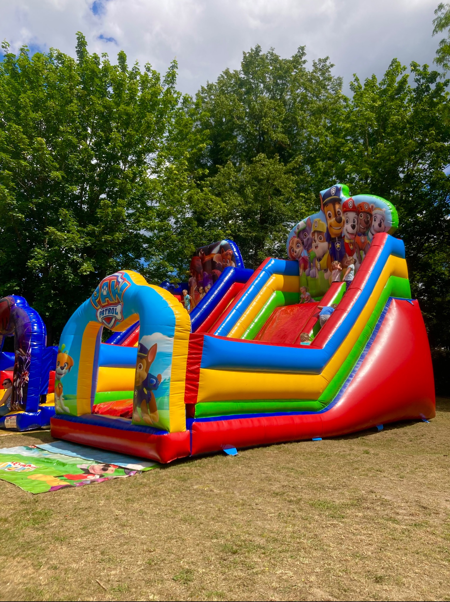 Kolorowy, dmuchany zamek ze zjeżdżalnią z motywem Paw Patrol na trawie w słoneczny dzień.