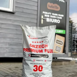 Worek z ekogroszkiem 'Orzech Premium Plus' 25 kg, z widocznymi informacjami o granulacji, wartości opałowej i zawartości siarki, ustawiony przed budynkiem biura firmy 'Ecopal' z godzinami otwarcia.