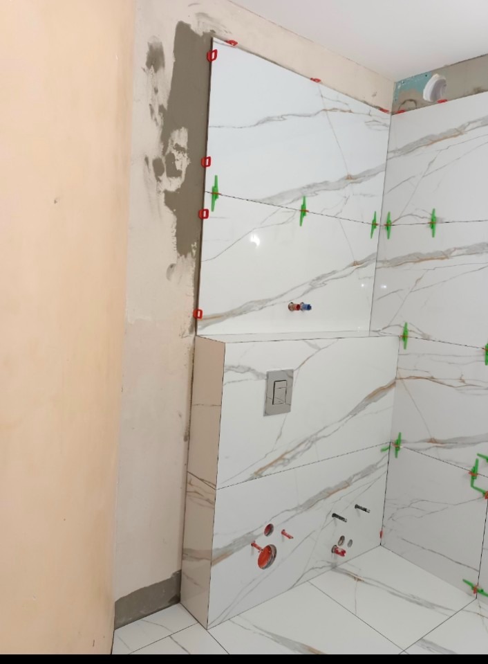 Ściana łazienki w trakcie układania białych płytek imitujących marmur, widoczne krzyżyki dystansowe i resztki zaprawy na sąsiedniej ścianie.