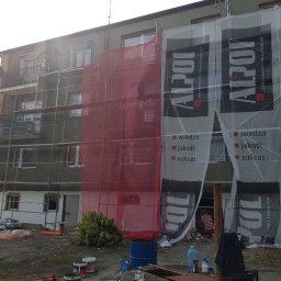 MW TRAST SPÓŁKA Z OGRANICZONĄ ODPOWIEDZIALNOŚCIĄ - Budynek wielorodzinny w trakcie prac elewacyjnych z użyciem rusztowania i siatki ochronnej, widoczne materiały budowlane i reklama firmy Alpol.