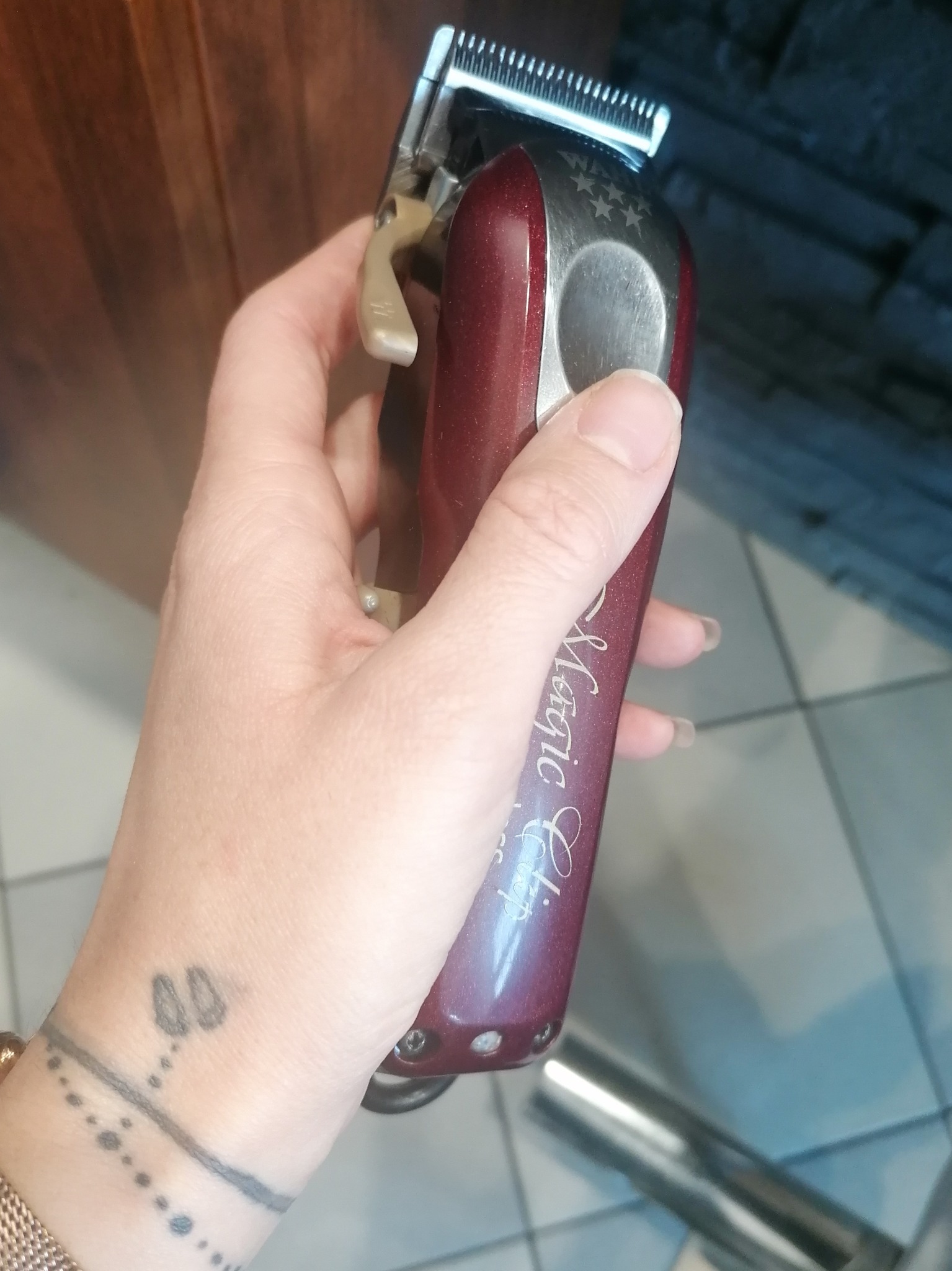 Dłoń z tatuażem trzyma maszynkę do strzyżenia włosów marki Wahl Magic Clip, widoczne metalowe ostrze i burgundowa obudowa z napisem.