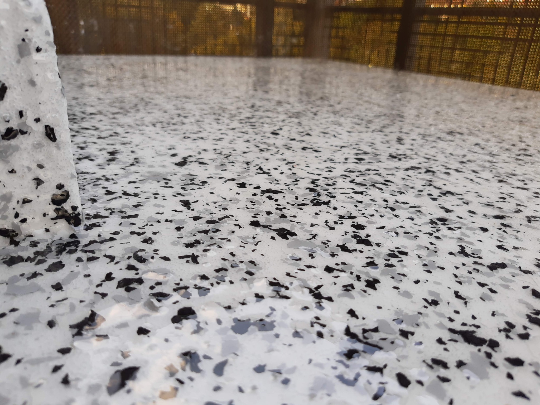 Szara, błyszcząca powierzchnia z czarnymi i białymi elementami dekoracyjnymi, prawdopodobnie na balkonie, z widoczną metalową balustradą w tle.